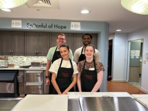 4 associates wearing aprons in a food prep kitchen. 